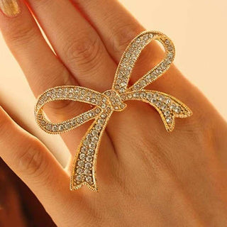 A hand wearing a large, gold bow-shaped ring adorned with shiny stones, echoing the elegance of exquisite earrings for women.